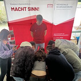 Fünf Schülerinnen und Schüler des Gymnasiums tummeln sich um den Tisch des Messestands unserer Hochschule, um gemeinsam ein Holzpuzzle zu lösen. 